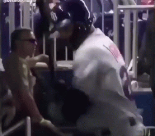 A Baseball Player Is Holding A Bat In A Stadium While A Man Looks On . GIF