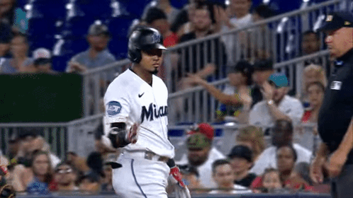 A Baseball Player Is Running Towards The Dugout While A Referee Watches . GIF