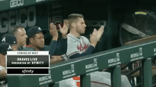 A Baseball Player Is Sitting In The Dugout Applauding His Team . GIF