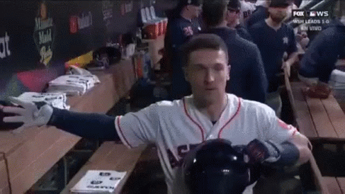 A Baseball Player Is Standing In A Dugout With His Arms Outstretched And Holding A Helmet . GIF