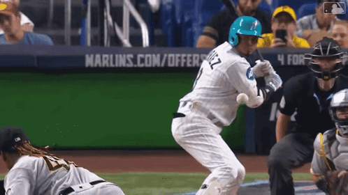 A Baseball Player Is Swinging At A Ball In Front Of A Marlins.com/offers Sign GIF