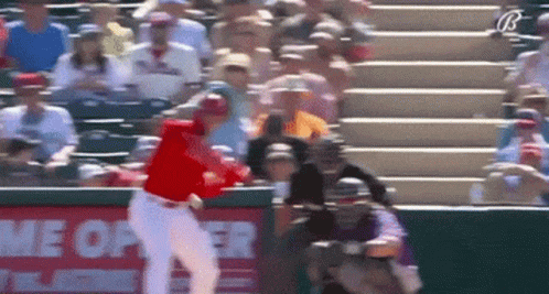A Baseball Player Is Swinging At A Ball In Front Of A Sign That Says Home Opener GIF