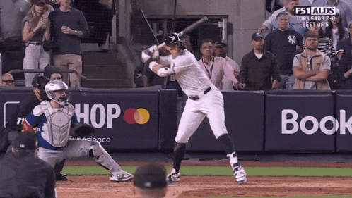 A Baseball Player Is Swinging At A Pitch In Front Of A Wall That Says Hop And Book GIF