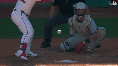 A Baseball Player Is Swinging His Bat At A Ball While The Catcher Watches GIF