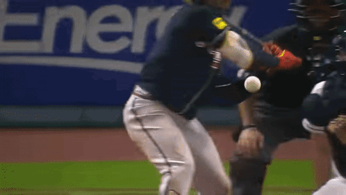 A Baseball Player Swings A Bat At A Ball While A Catcher Looks On GIF