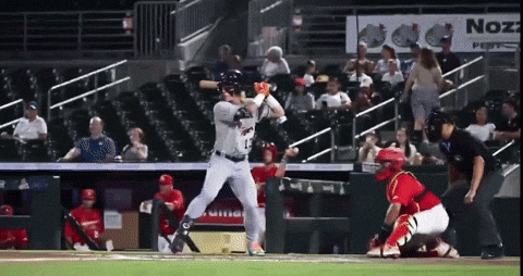A Baseball Player Swings At A Pitch In Front Of An Advertisement For Nozz GIF