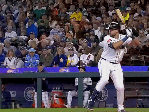 A Baseball Player Swings His Bat At A Ball In Front Of A Crowd With A Banner That Says Coca Cola GIF
