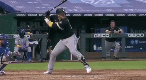 A Baseball Player Swings His Bat At A Ball In Front Of A Geico Sign GIF