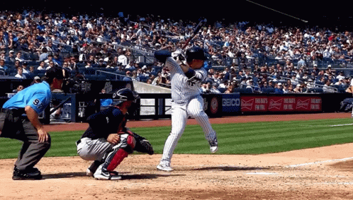 A Baseball Player Swings His Bat At A Pitch In Front Of A Seico Ad GIF