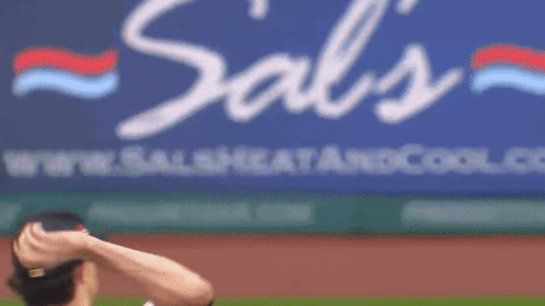 A Baseball Player Throws A Ball In Front Of A Cool.com Sign GIF