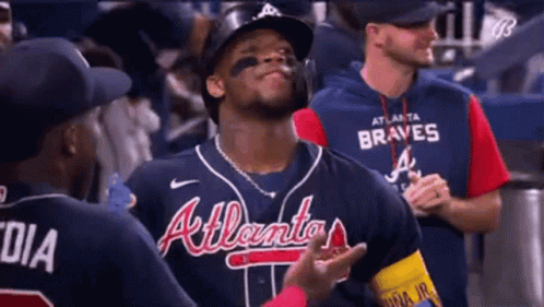 A Baseball Player Wearing A Braves Jersey Is Standing In The Dugout Talking To His Teammates . GIF