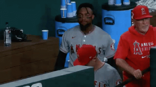 A Baseball Player Wearing A Gray Angels Jersey Is Sitting In The Dugout . GIF