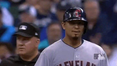 A Baseball Player Wearing A Helmet And A Cleveland Jersey Stands In Front Of A Referee . GIF