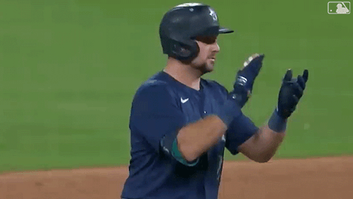 A Baseball Player Wearing A Helmet And Gloves Is Clapping His Hands On The Field . GIF