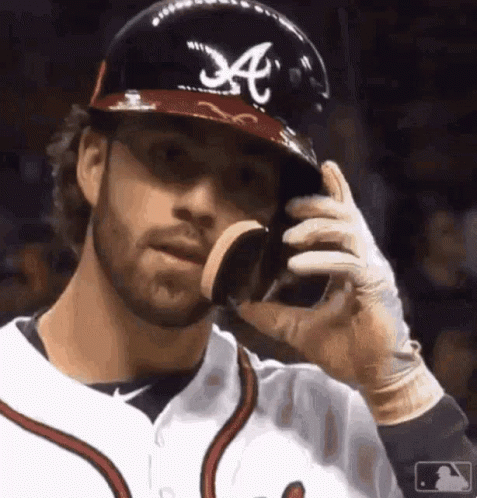 A Baseball Player Wearing A Helmet With The Letter A On It Is Eating A Cookie . GIF