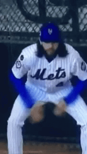A Baseball Player Wearing A Mets Jersey And A Blue Hat Is Squatting Down On The Field . GIF