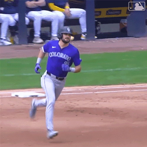 A Baseball Player Wearing A Purple Colorado Jersey Is Running To First Base . GIF