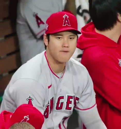 A Baseball Player Wearing A Red Hat And A White Jersey Is Sitting In A Dugout . GIF