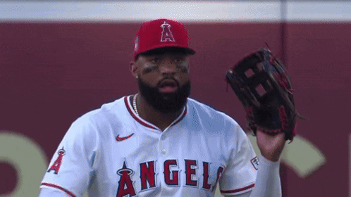 A Baseball Player Wearing A Red Hat And A White Jersey With The Word Angels On It Is Holding A Glove In His Hand . GIF