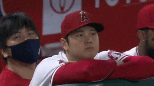 A Baseball Player Wearing A Red Hat And A White Shirt Is Sitting In The Dugout With His Arms Crossed . GIF