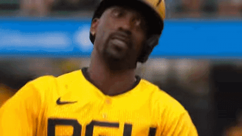 A Baseball Player Wearing A Yellow Jersey And A Helmet Is Looking Up At The Sky . GIF