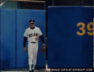 A Baseball Player With The Number 99 On His Jersey Stands In Front Of A Blue Wall GIF