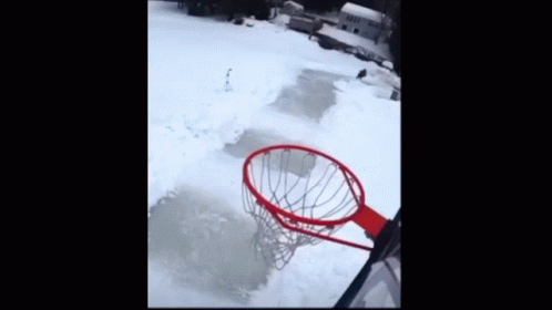 A Basketball Is Going Through A Hoop In The Snow With A House In The Background GIF