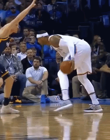 A Basketball Player Dribbles The Ball While Another Player Tries To Stop Him GIF