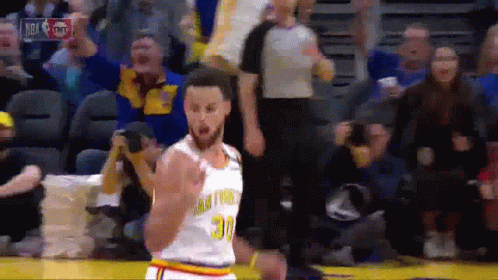 A Basketball Player In A Golden State Warriors Uniform Is Standing On The Court In Front Of A Crowd . GIF