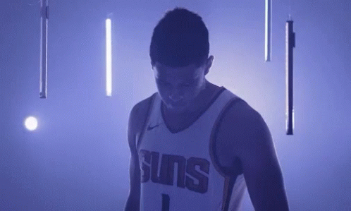A Basketball Player In A Suns Jersey Is Standing In A Dark Room With Purple Lights . GIF