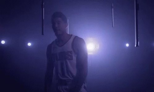 A Basketball Player In A Suns Jersey Is Standing In A Dark Room . GIF