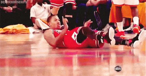 A Basketball Player Is Laying On His Back On The Floor While A Crowd Watches . GIF