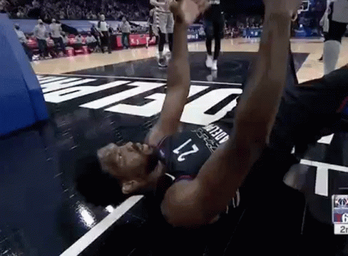 A Basketball Player Is Laying On The Floor Of A Basketball Court . GIF