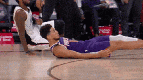 A Basketball Player Is Laying On The Floor While Another Player Sits On The Bench GIF