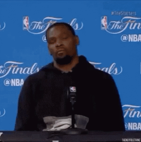 A Basketball Player Is Sitting At A Table In Front Of A Microphone With His Eyes Closed . GIF