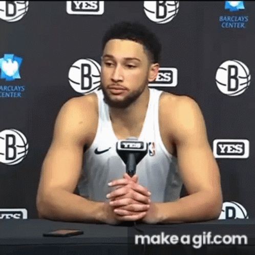 A Basketball Player Is Sitting At A Table With A Microphone In Front Of Him . GIF