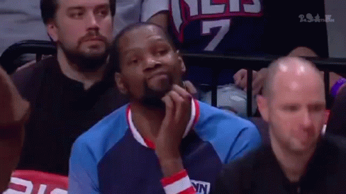 A Basketball Player Is Sitting In The Stands During A Game And Looking At Something . GIF