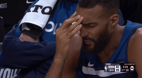 A Basketball Player Is Sitting In The Stands With His Hand On His Forehead During A Game GIF