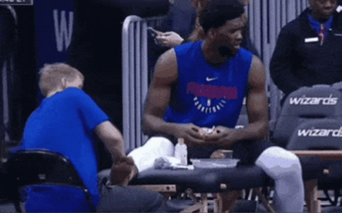 A Basketball Player Is Sitting On A Bench Talking To A Child . GIF