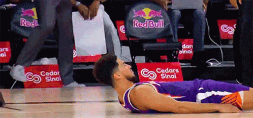 A Basketball Player Laying On The Floor In Front Of A Red Bull Ad GIF