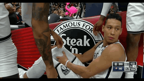 A Basketball Player Laying On The Floor With A Steak 'N Advertisement In The Background GIF