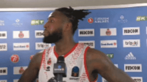 A Basketball Player Stands In Front Of A Blue Wall With Turkish Airlines And Fedecom Logos On It GIF