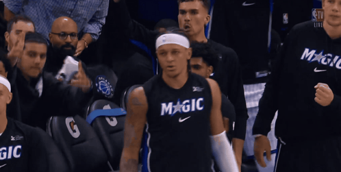 A Basketball Player Wearing A Black Magic Jersey Stands In Front Of A Crowd GIF