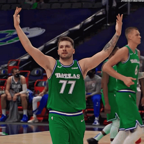 a basketball player wearing a dallas 77 jersey is raising his arms in the air