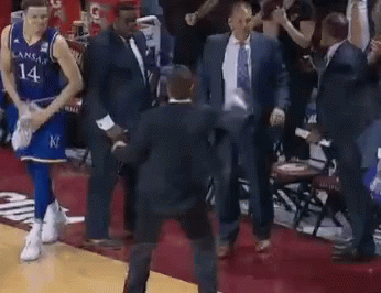 A Basketball Player Wearing A Kansas Jersey Is Walking On The Court With A Group Of Men . GIF