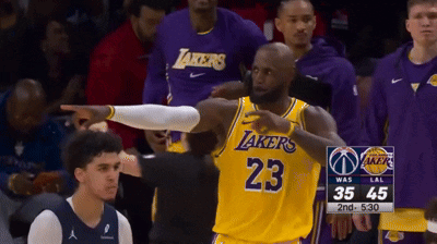 a basketball player wearing a lakers jersey points at someone