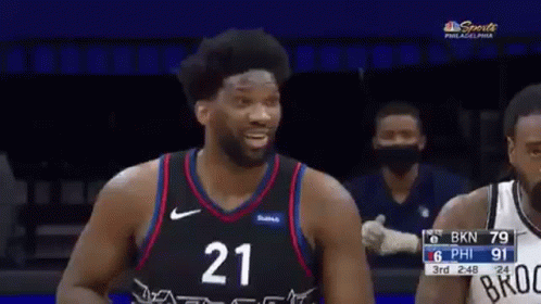 A Basketball Player Wearing A Number 21 Jersey Is Laughing While Standing Next To Another Player . GIF