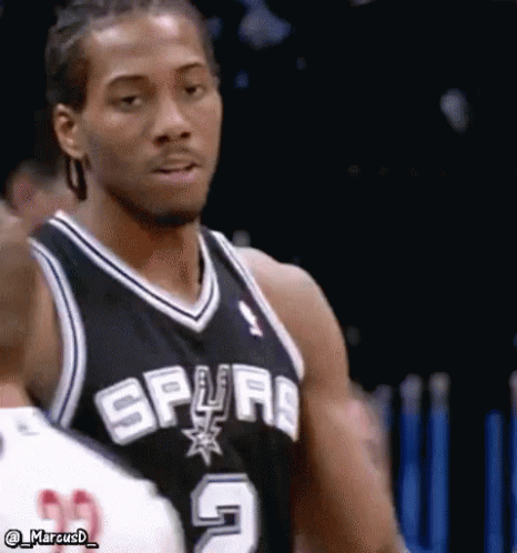 A Basketball Player Wearing A Spurs Jersey Is Standing In Front Of A Fence . GIF
