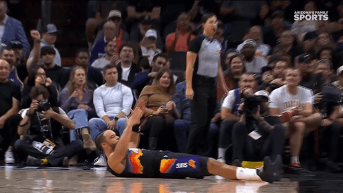 A Basketball Player Wearing A Suns Uniform Is Laying On The Floor GIF
