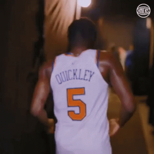 A Basketball Player Wearing A White Jersey With The Number 5 On It Is Walking Down A Hallway . GIF
